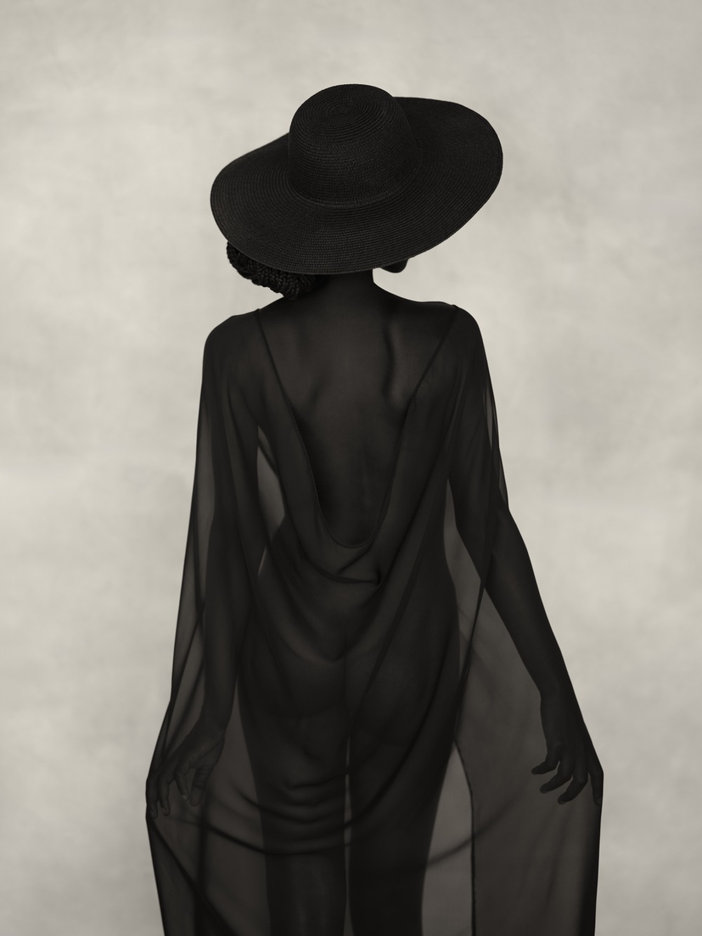 A figure standing with their back to the camera, wearing a flowing sheer black cover-up and a black hat, with their arms relaxed at their sides.